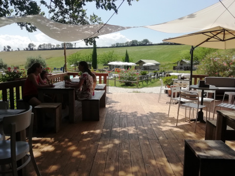 Terraza de madera con mesas y sombrillas en Tenuta Tredici Ulivi, parque vacacional en Marche, Italia.