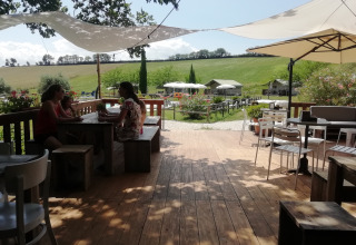 Træterrasse med borde og parasoller på Tenuta Tredici Ulivi feriepark i Marche, Italien, sommerdag.