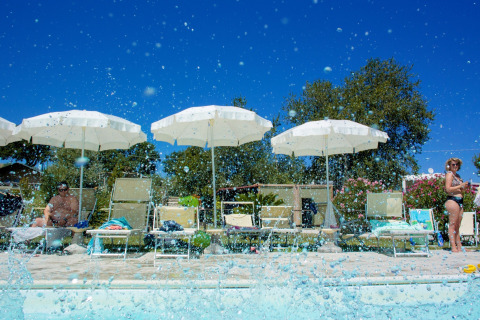 Zona de piscina con tumbonas y sombrillas en Tenuta Tredici Ulivi, parque vacacional en Marche, Italia, al sol.