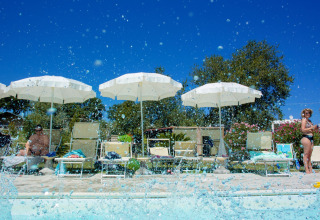 Poolbereich mit Sonnenliegen und Sonnenschirmen im Ferienpark Tenuta Tredici Ulivi in Marche, Italien, bei Sonne.