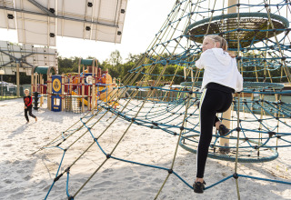 Kinderen ravotten op het zand van de speeltuin met klimnet bij Recreatieoord Wilhelm Tell, Limburg, België.