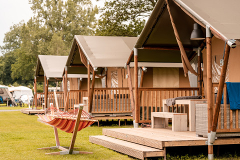 Fila de tiendas glamping con terrazas y una hamaca en el parque Recreatieoord Wilhelm Tell, Bélgica.