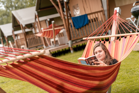 Een vrouw ontspant met een boek in een kleurrijke hangmat bij Wilhelm Tell vakantiedomein in Limburg.