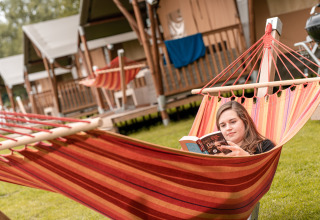 Een vrouw ontspant met een boek in een kleurrijke hangmat bij Wilhelm Tell vakantiedomein in Limburg.