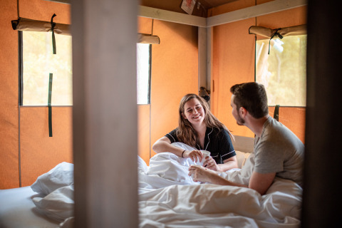 Pareja relajándose en la cama con café en una acogedora cabaña en Recreatieoord Wilhelm Tell, Bélgica.