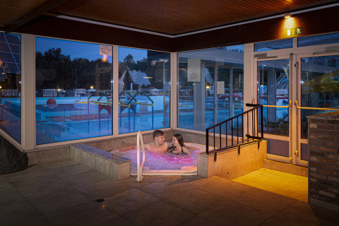 Una pareja disfruta en un jacuzzi interior con vista a la piscina en Recreatieoord Wilhelm Tell en Limburg, Bélgica.