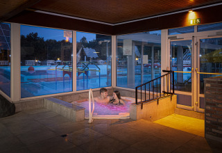 Et par nyder en jacuzzi indendørs med udsigt til poolområde på Recreatieoord Wilhelm Tell i Limburg, Belgien.