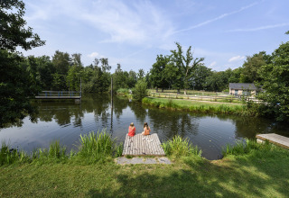 Zwei Kinder sitzen auf einem Holzsteg an einem Teich im Recreatiepark de Lucht in Utrecht, Niederlande.