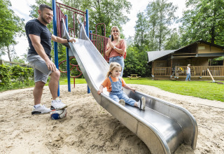 Familie leger på legepladsen med rutsjebane ved et feriepark i Utrecht, Holland, omgivet af grøn natur.