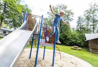 Dreng hopper fra legepladsudstyr ved siden af en rutsjebane i ferieparken Recreatiepark de Lucht, Utrecht.