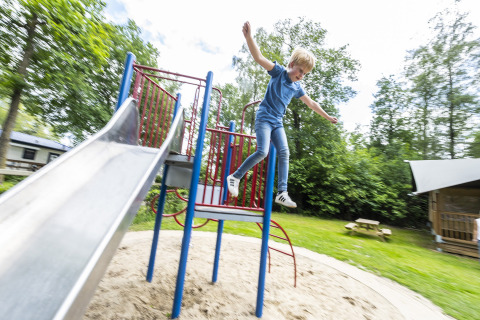Jongen springt van klimrek naast glijbaan op de speeltuin van Recreatiepark de Lucht in Utrecht, Nederland.