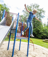 Junge springt von einem Klettergerüst neben einer Rutsche im Recreatiepark de Lucht in Utrecht, Niederlande.