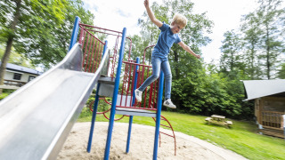 Jongen springt van klimrek naast glijbaan op de speeltuin van Recreatiepark de Lucht in Utrecht, Nederland.