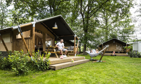 Gezin geniet buiten bij safaritenten met hangmat op het groene Recreatiepark de Lucht in Utrecht.