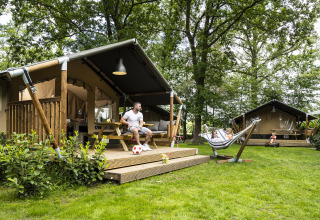 People relaxing outside safari tents with a hammock and lush greenery at Recreatiepark de Lucht, Utrecht.