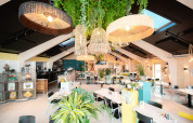 Lys og moderne café med grønne planter, hængende lamper og naturligt lys i Vakantiepark De Nollen, Holland.