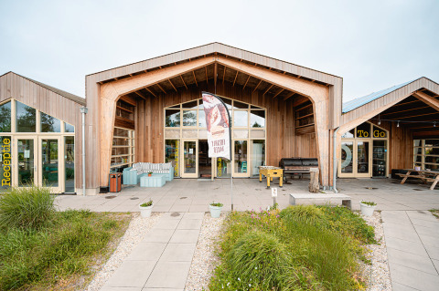 Modern wooden building at the entrance of Vakantiepark De Nollen in North Holland, Netherlands, with greenery.