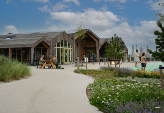 Vakantiepark De Nollen in Noord-Holland, Nederland, met mensen, bloemenperk en modern houten gebouw.