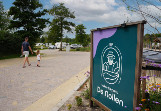 Ein Mann und ein Kind spazieren durch den Vakantiepark De Nollen in Nordholland, Niederlande, mit Wohnwagen im Hintergrund.