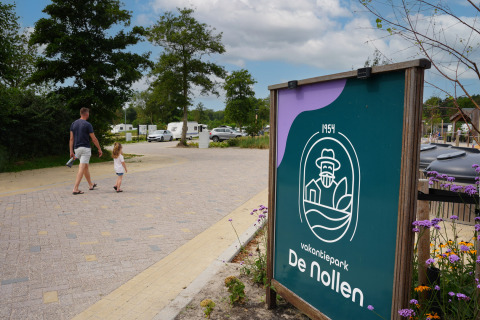 Ein Mann und ein Kind spazieren durch den Vakantiepark De Nollen in Nordholland, Niederlande, mit Wohnwagen im Hintergrund.