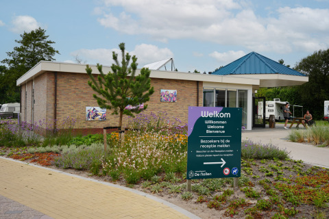 Entrada al Vakantiepark De Nollen en Holanda Septentrional, Países Bajos, con letrero de bienvenida y edificio moderno.