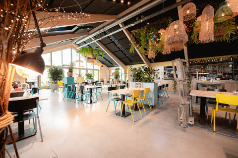 Bright, modern restaurant with green plants and colorful chairs at Vakantiepark De Nollen, North-Holland.
