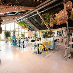 Licht en modern restaurant met planten en kleurrijke stoelen in Vakantiepark De Nollen, Noord-Holland.