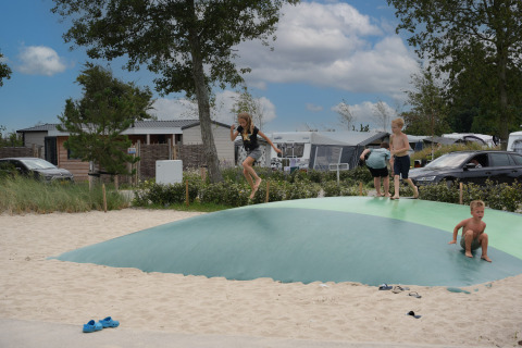 Kinder spielen auf einem aufblasbaren Kissen im Sand im Vakantiepark De Nollen, Nordholland, Niederlande.