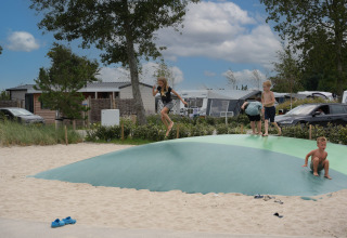 Kinder spielen auf einem aufblasbaren Kissen im Sand im Vakantiepark De Nollen, Nordholland, Niederlande.