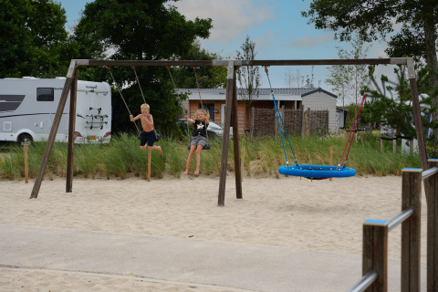 Kinder schaukeln auf einem Spielplatz mit Sand bei Vakantiepark De Nollen in Nordholland, Niederlande.