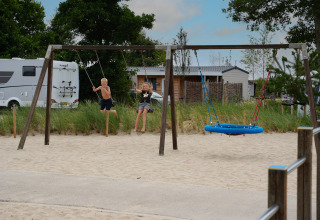 Kinder schaukeln auf einem Spielplatz mit Sand bei Vakantiepark De Nollen in Nordholland, Niederlande.