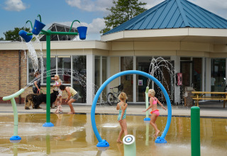 Kinder spielen an einem Wasserspielplatz vor einem Gebäude im Vakantiepark De Nollen, Nordholland, Niederlande.