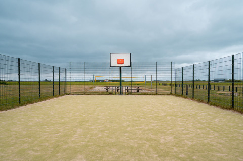 Außen-Basketballfeld mit Zaun, Volleyballfeld und Picknicktisch im Ferienpark De Nollen, Niederlande.