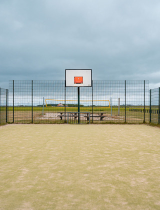 Außen-Basketballfeld mit Zaun, Volleyballfeld und Picknicktisch im Ferienpark De Nollen, Niederlande.