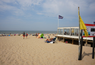 Beach scene at Vakantiepark De Nollen in North Holland, Netherlands, with people and a beach pavilion.