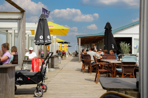 Außenbereich im Vakantiepark De Nollen, Nordholland, Niederlande, mit Gästen unter farbigen Sonnenschirmen.