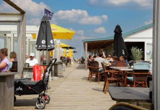 Außenbereich im Vakantiepark De Nollen, Nordholland, Niederlande, mit Gästen unter farbigen Sonnenschirmen.