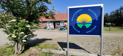 Welcome sign at Ballum Camping holiday park in Southern Denmark, with building and flowering tree.