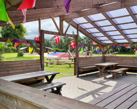 Zona de descanso al aire libre en Ballum Camping, Dinamarca, con banderas danesas y guirnaldas de colores.