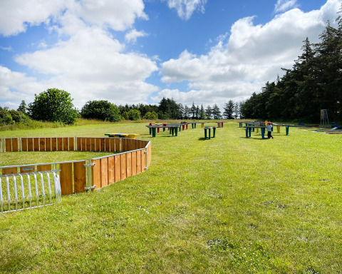 Buitenspeelplaats met kleurrijke tafels en houten bouwwerken op gras bij Ballum Camping, Zuid-Denemarken.