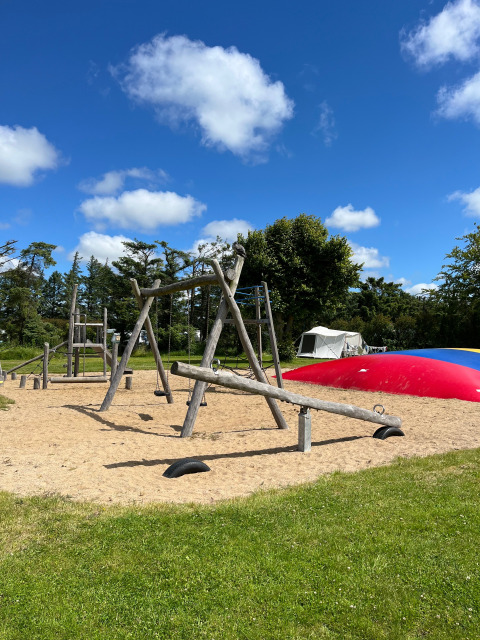 Speelplaats met schommels en wipwap bij Ballum Camping in Zuid-Denemarken onder een blauwe lucht.