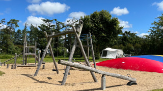 Parque infantil con columpios y balancines en Ballum Camping, Dinamarca, bajo un cielo azul y soleado.