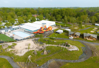 Aerial view of a campsite with safari tents, pool, waterslide, playground equipment and green scenery.