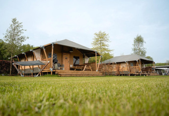 Tienda safari Villatent Cottage en Holiday Park Ackersate, Países Bajos, con césped y terraza de madera.