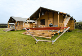 Tente safari Villatent Nomad au Holiday Park Ackersate aux Pays-Bas, avec terrasse en bois et hamac rouge.