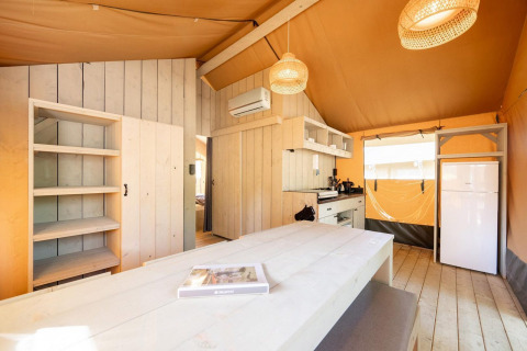 Interior de una tienda safari Villatent Nomad en Holiday Park Ackersate, Países Bajos, con cocina y mesa.