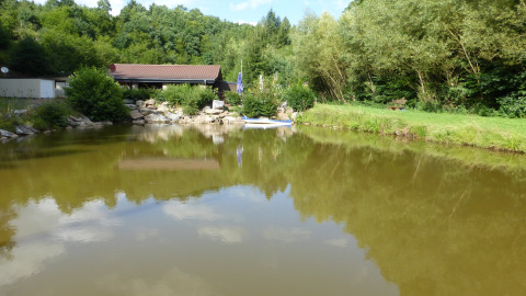 Teich im Camping Bockenauer Schweiz mit Bäumen, Wiese und Ferienhaus in Rheinland-Pfalz, Deutschland.
