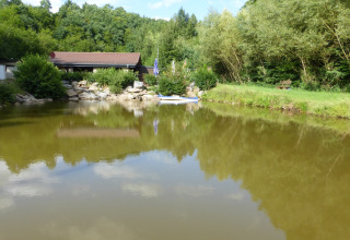 Pond at Camping Bockenauer Schweiz with lush greenery, trees, and a holiday home in Rhineland-Palatinate, Germany.
