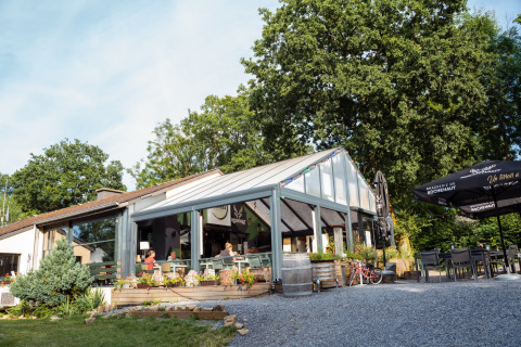 Area esterna di un caffè al Camping de Chênefleur, parco vacanze in Lussemburgo, Belgio, con tavoli e alberi.
