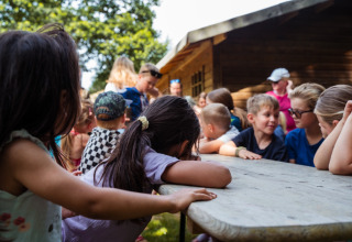 Børn samles rundt om et bord i solen ved Camping de Chênefleur i Belgisk Luxembourg, Belgien.